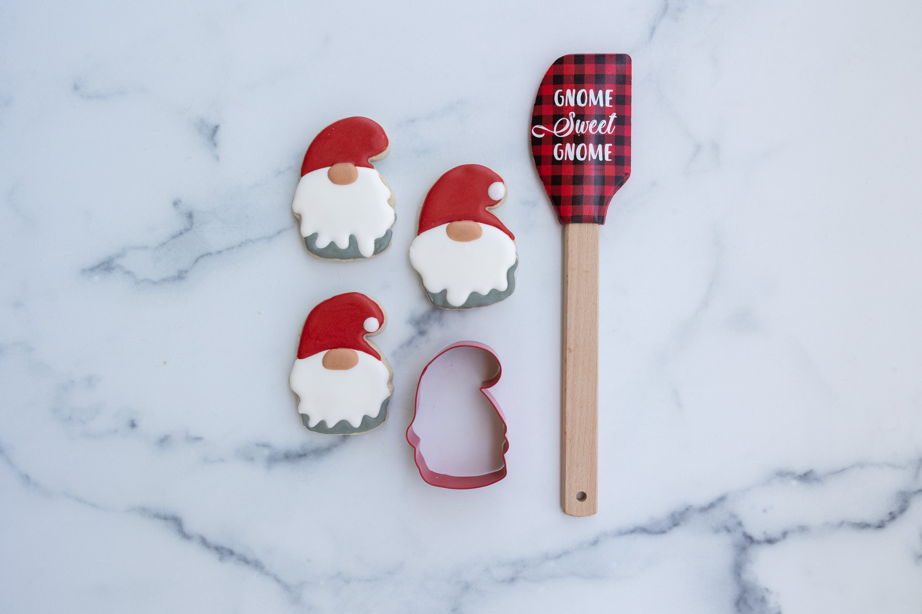 Lifestyle image of three completed gnome cookies with the gnome cookie cutter and spatula next to it 