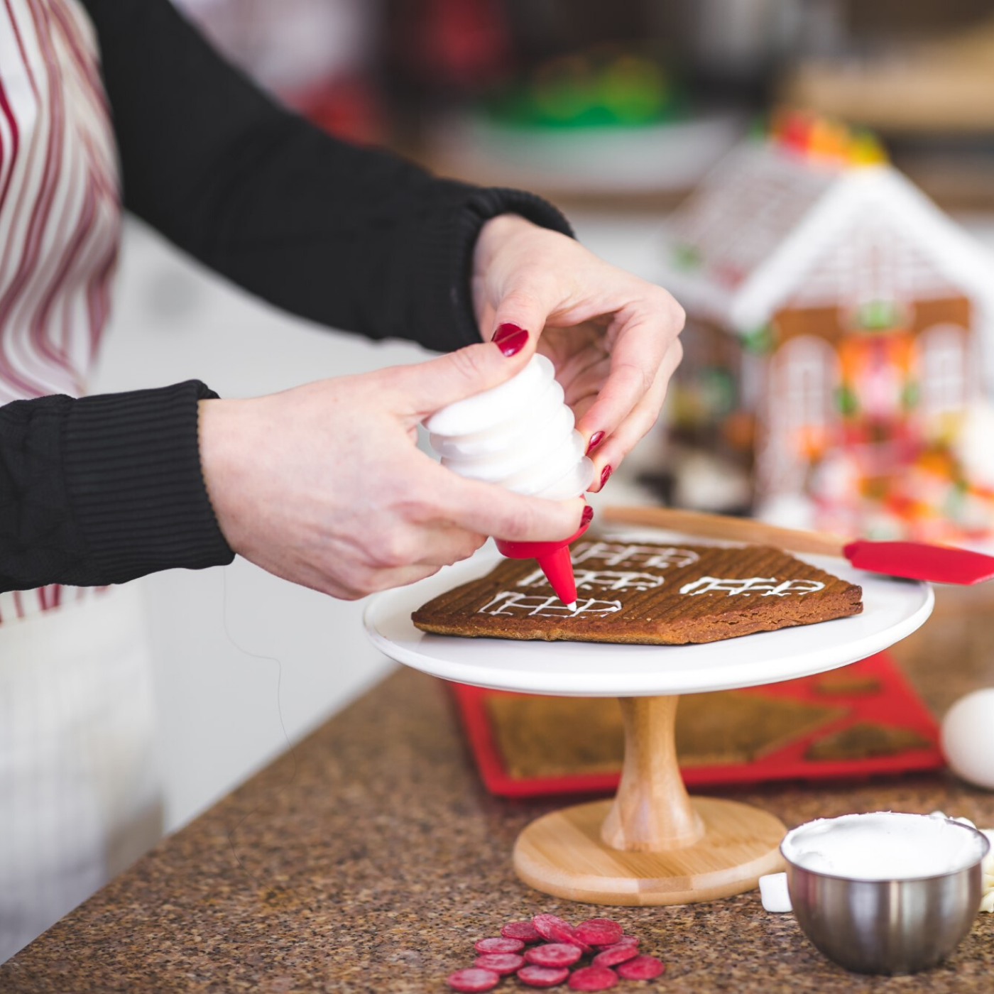 Lifestyle image of adult using frosting bottle to outline the shapes of windows on the gingerbread mold