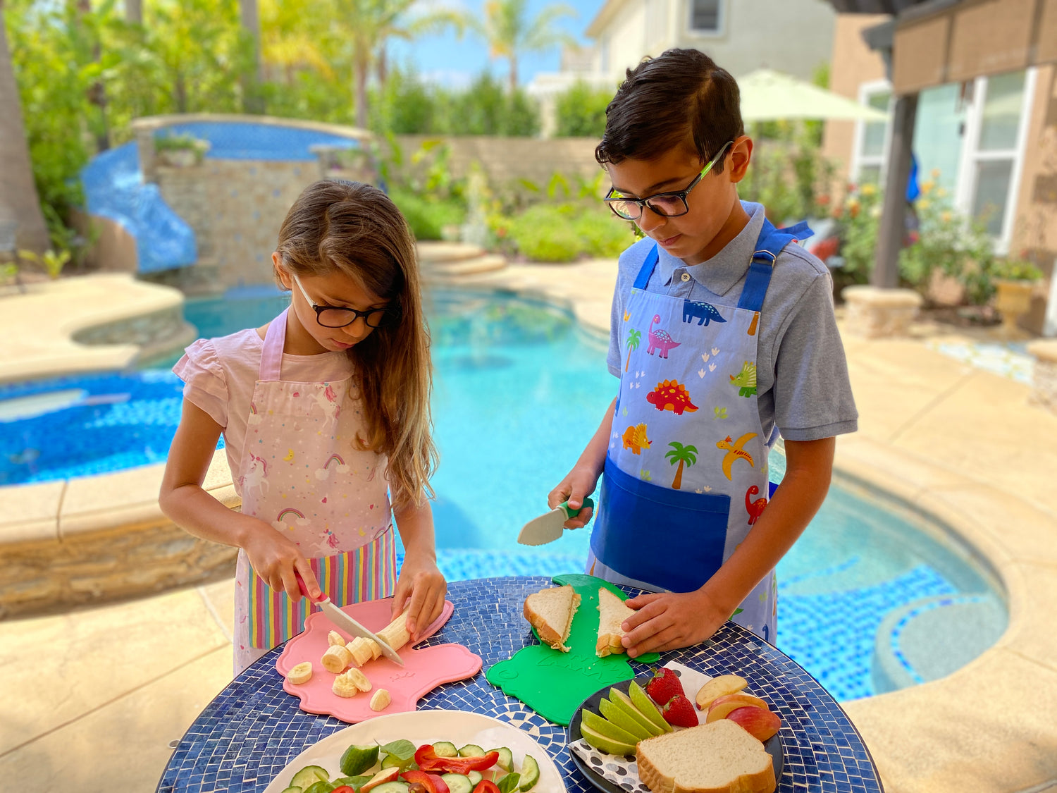 Lifestyle image of kids outside making sandwiches and snacks using the Dinosaur Cutting Board & Knife Set