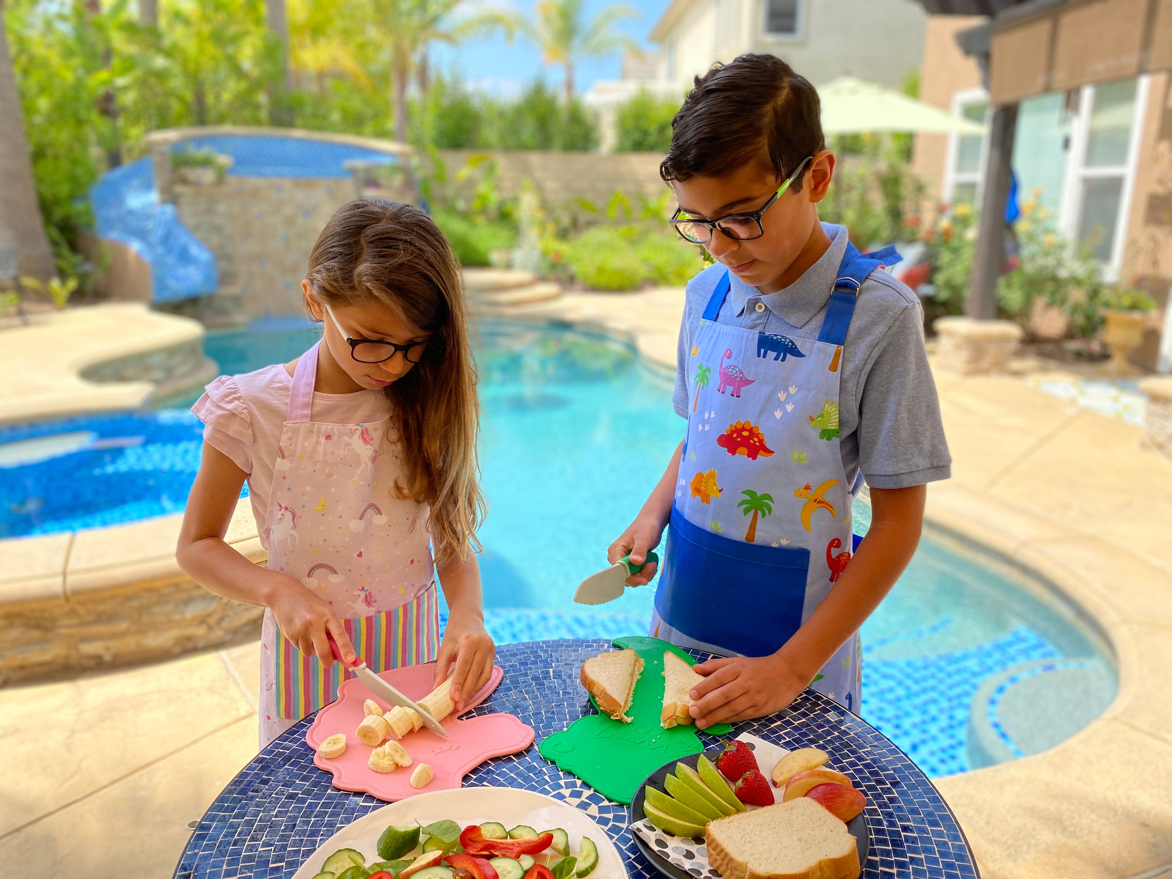 Lifestyle image of kids outside making sandwiches and snacks using the Dinosaur Cutting Board & Knife Set