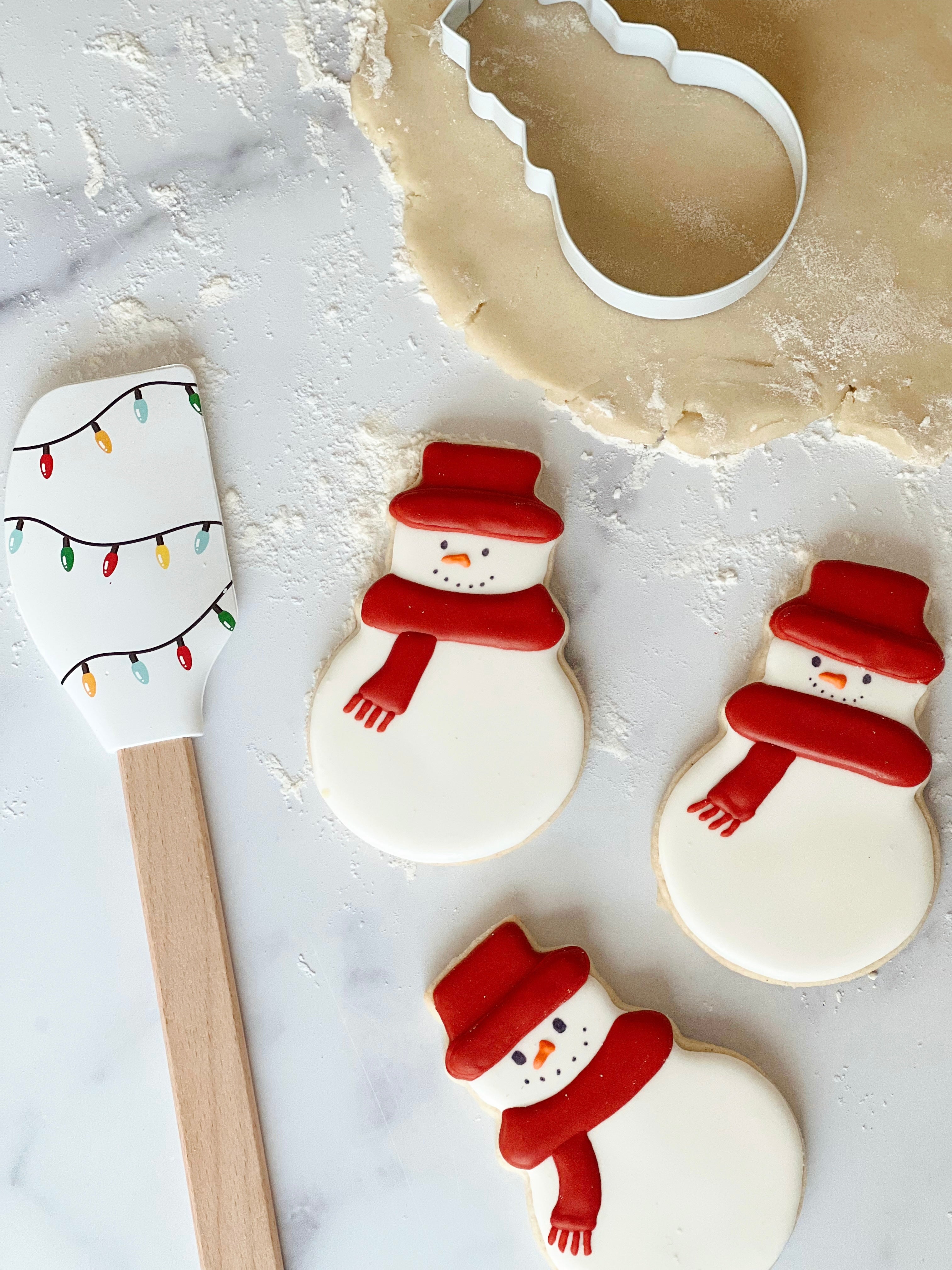 Lifestyle image of decorated snowman cookies next to a winter wonderland spatula