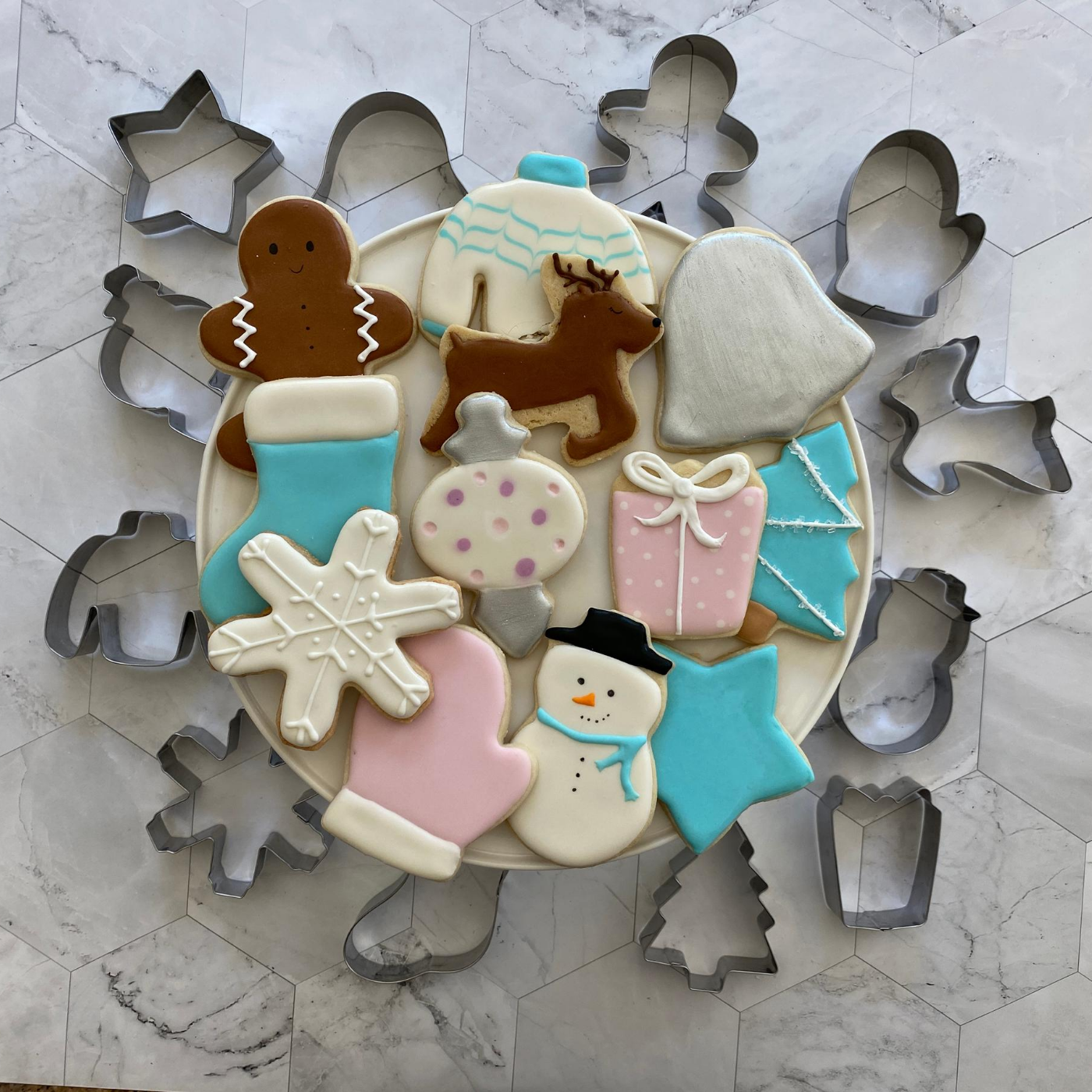Lifestyle image of completed winter wonderland cookies including a snowman, Christmas tree, snowflake, and more.