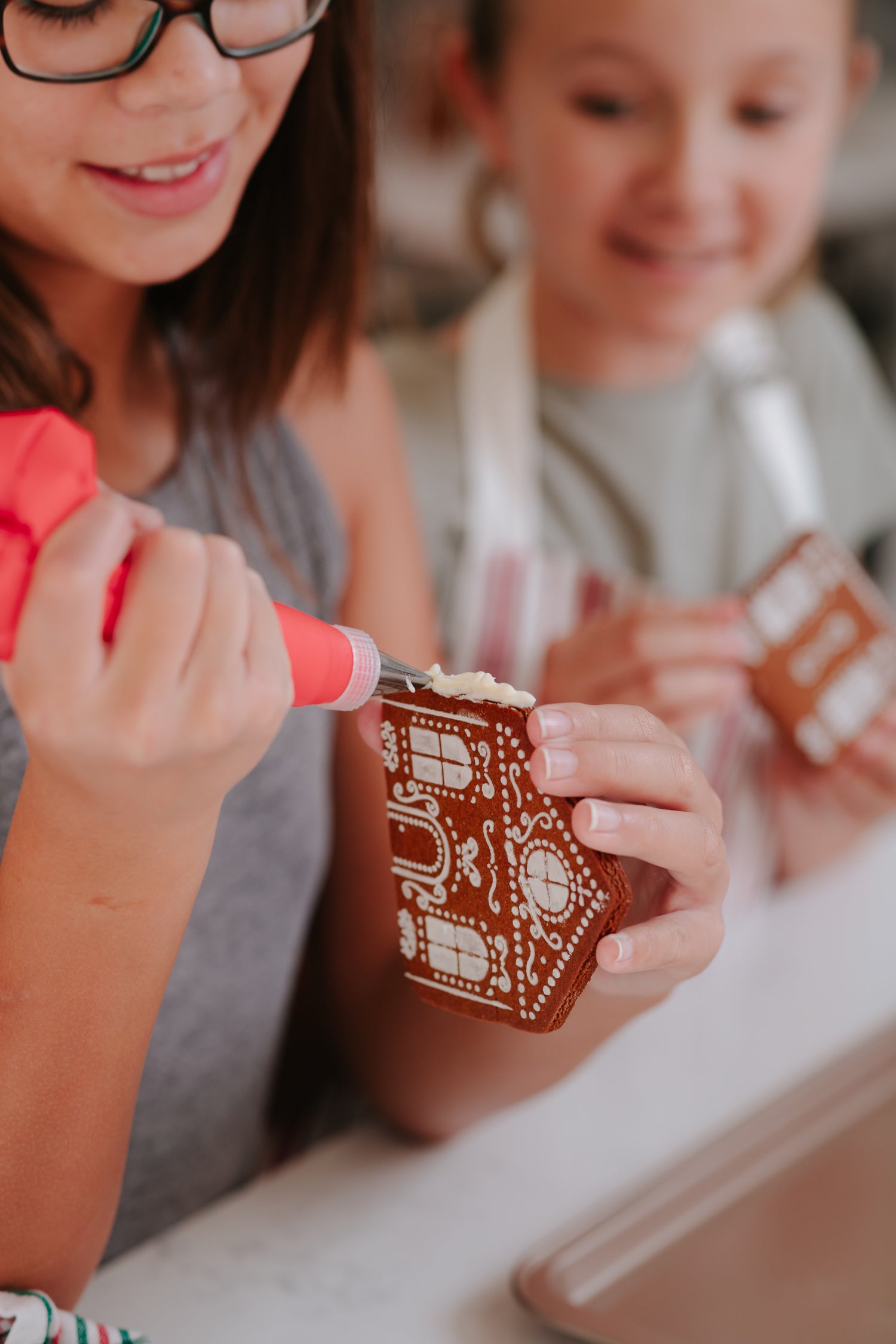 Lifestyle image of children decorating a wall of a gingerbread house from the "make your own gingerbread village set