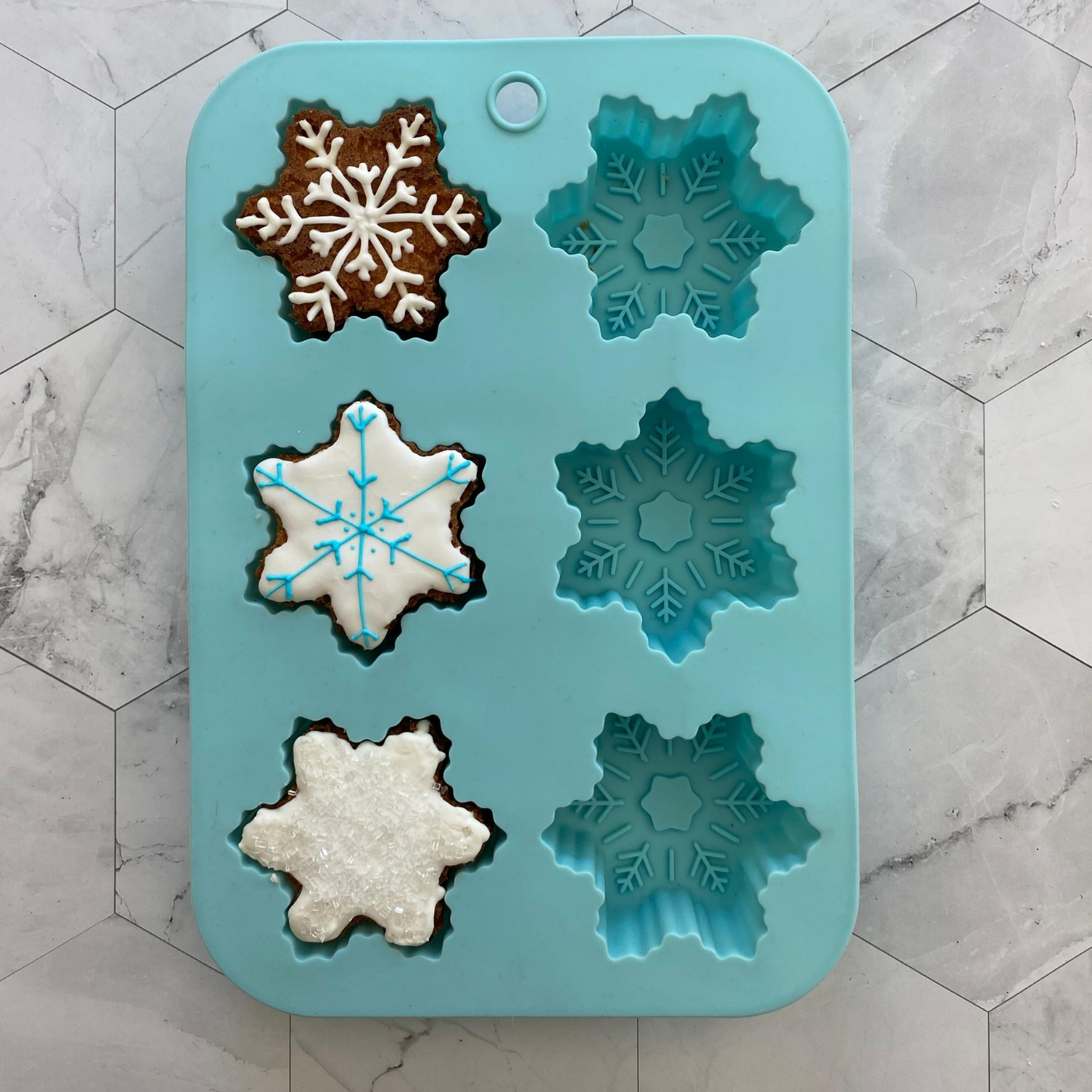 Lifestyle image of Winter Wonderland Snowflake Cupcake Mold with three decorated snowflake cupcakes