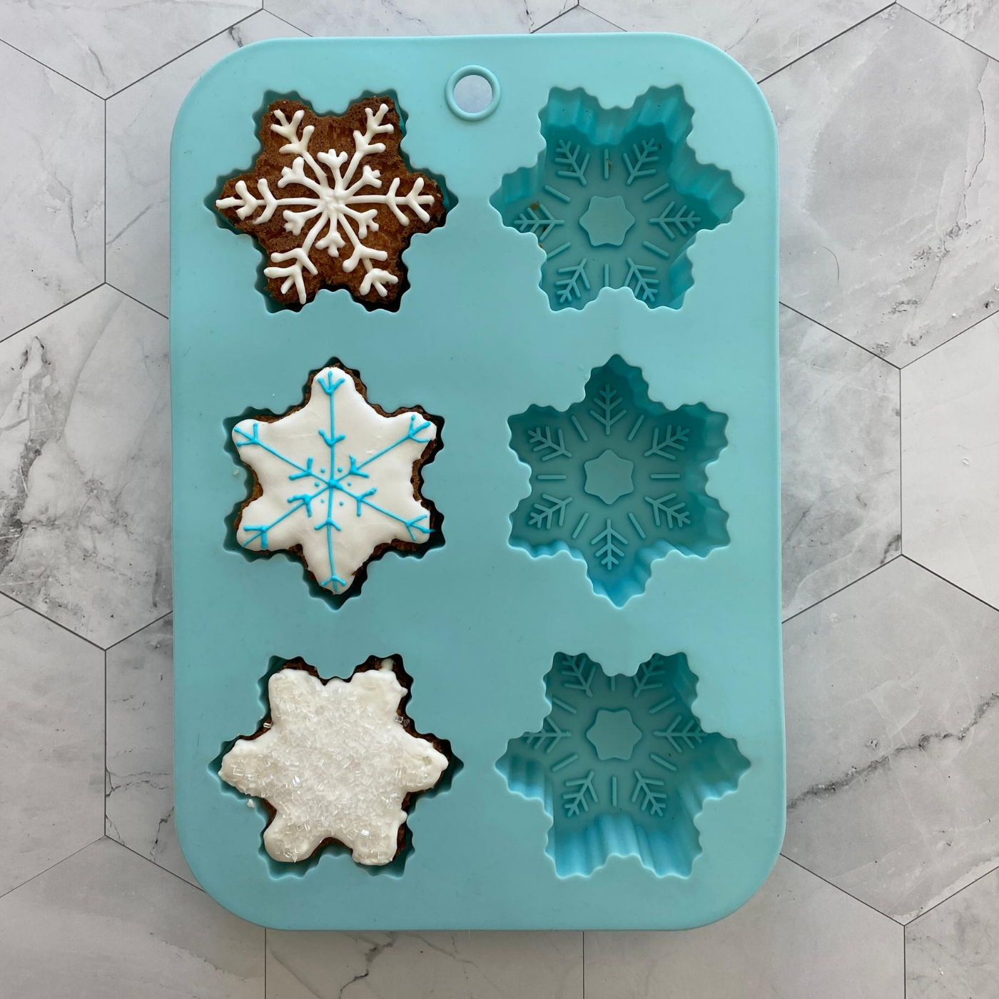 Lifestyle image of Winter Wonderland Snowflake Cupcake Mold with three decorated snowflake cupcakes 