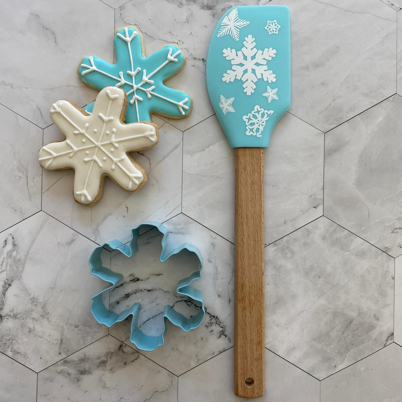 Lifestyle image of two completed snowflake cookies with the cookie cutter and spatula next to it 
