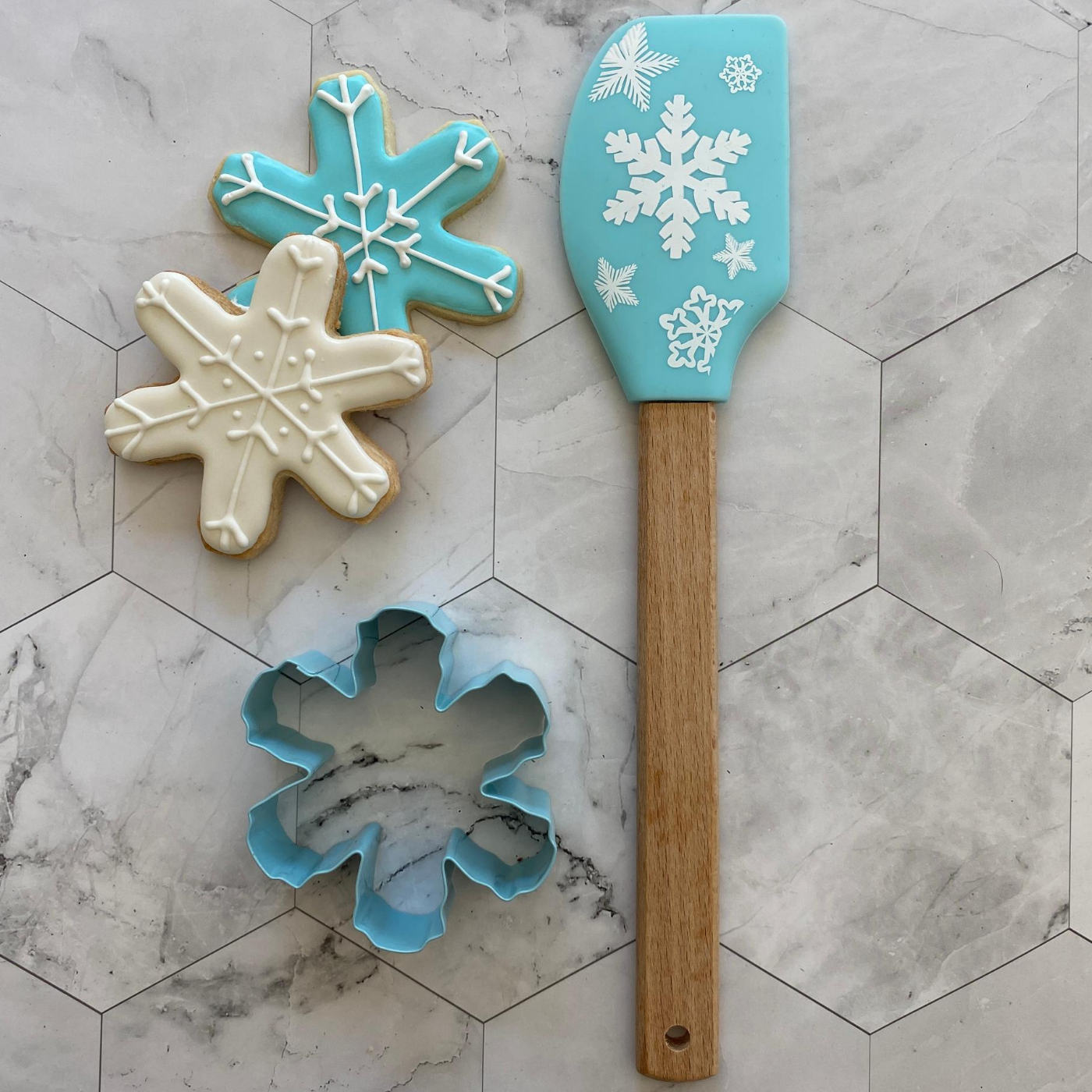 Lifestyle image of two completed snowflake cookies with the cookie cutter and spatula next to it