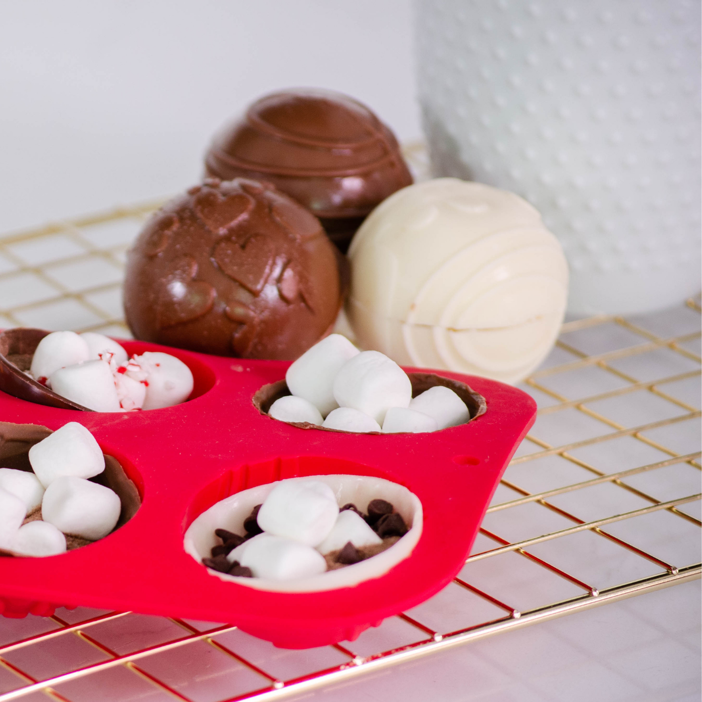 Lifestyle image of 3 complete hot cocoa bombs along with spheres half filled with cocoa bomb toppings such as marshmallows and chocolate chips 