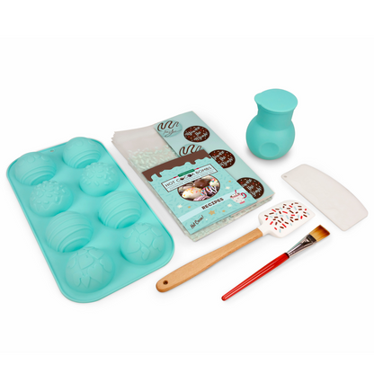 Out of box image of ultimate hot cocoa bomb set that includes  1 silicone mold to make 4 cocoa bombs, 1 silicone spatula, 1 chocolate scraper, 1 brush, 1 silicone melting pot with lid, 10 gift bags, stickers and recipes, plus QR code link to more exclusive recipes and videos.