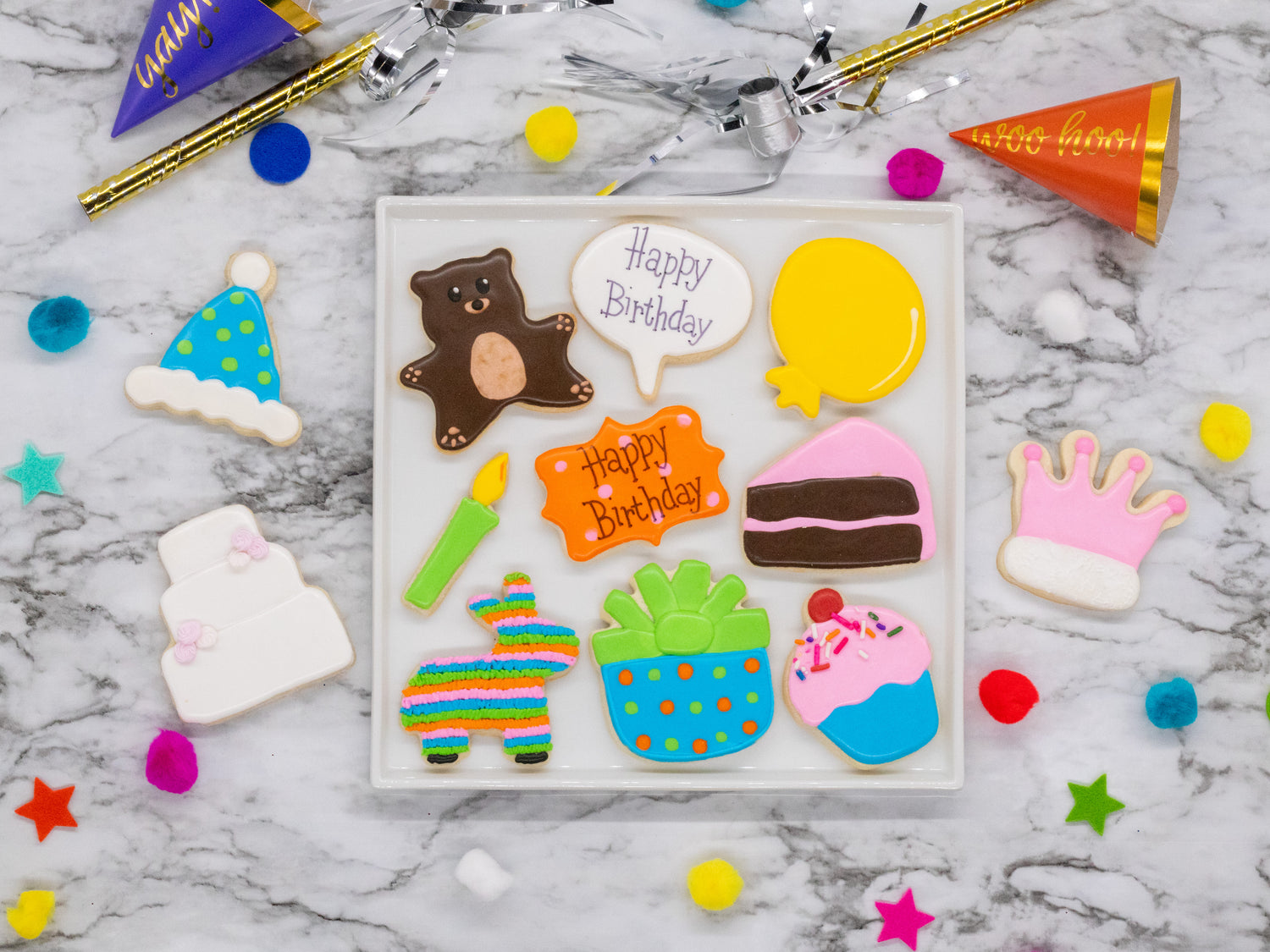 Lifestyle photo containing iced and decorated  Party hat, balloon, conversation bubble, donkey piñata,  cupcake, candle, cake slice, crown, teddy bear, happy birthday  plaque, gift and cake shaped cookies.