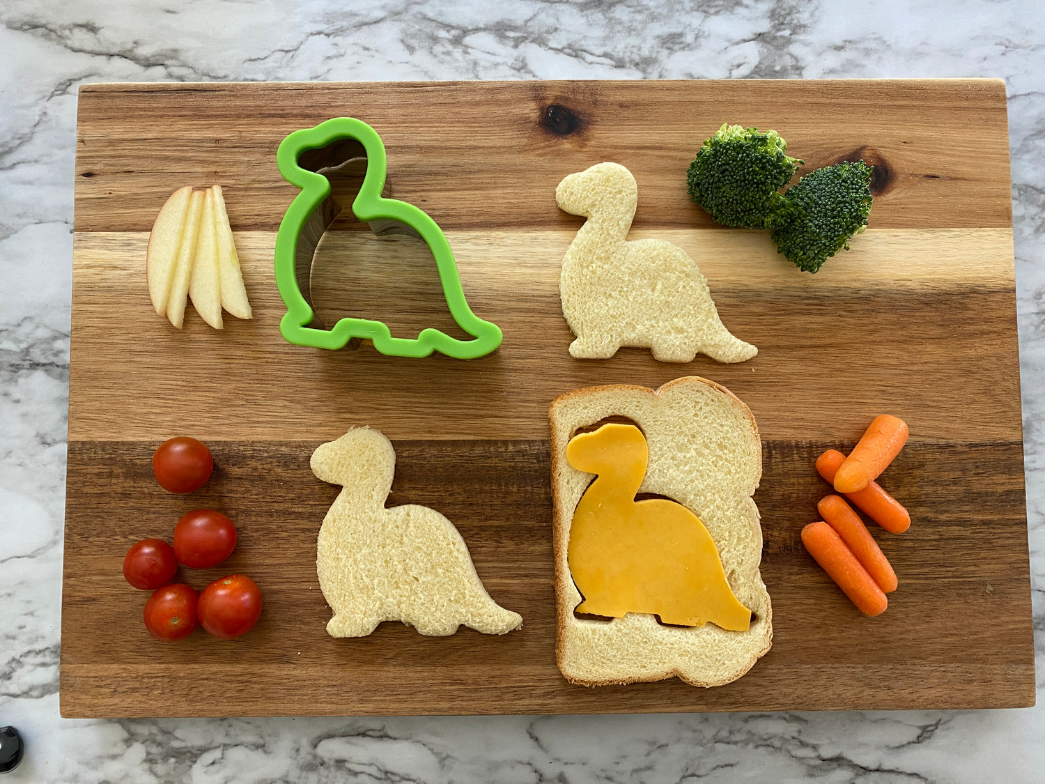 Lifestyle image of dinosaur shaped sandwiches and various snacks on a cutting board