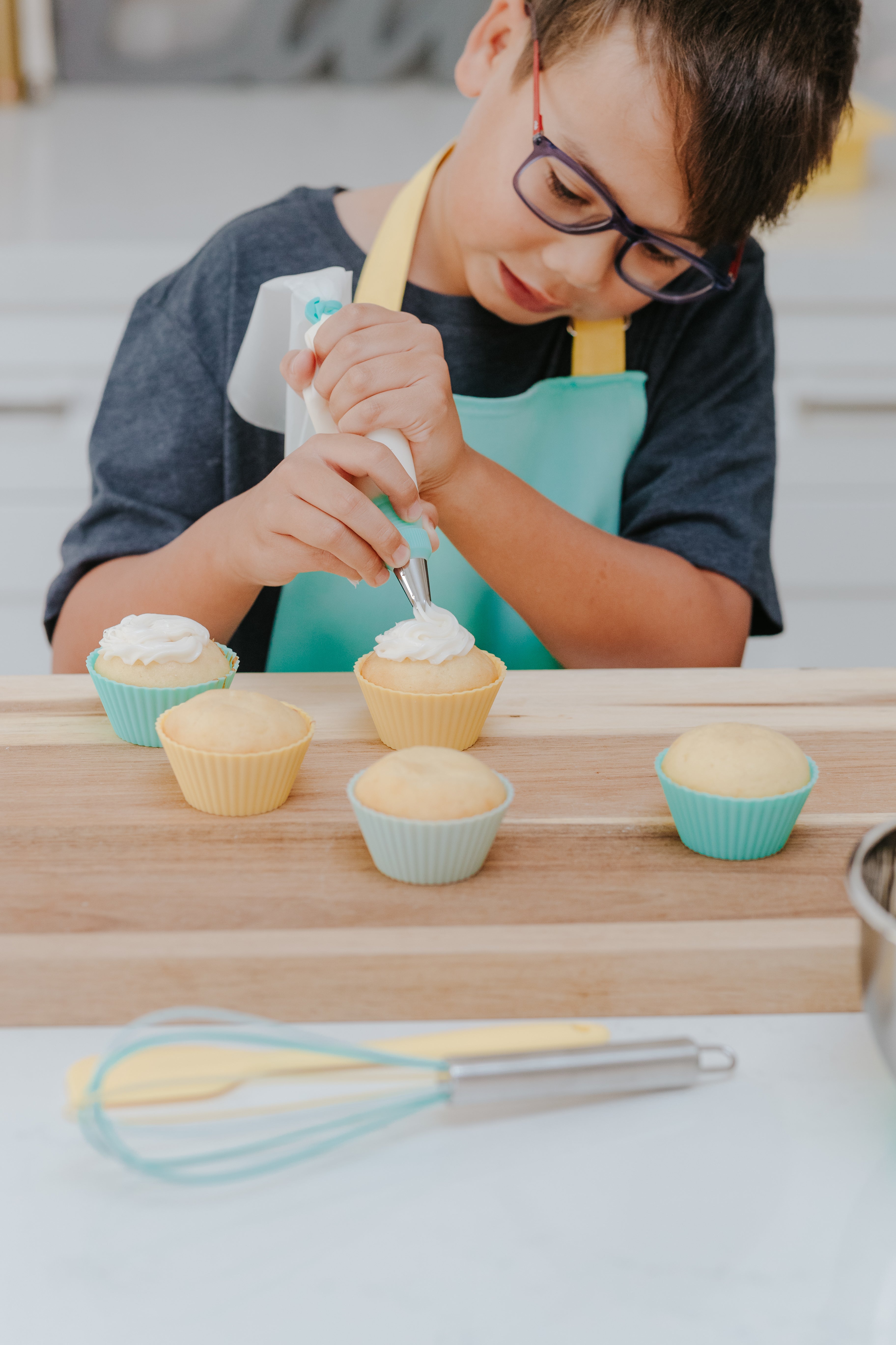 lifestyle image of young boy using the Classic Kids Baking Set to decorate cupcakes