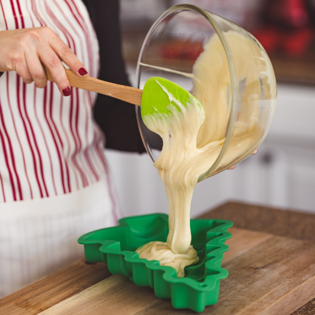 Adult using spatula to pour cake batter into holiday tree cake mold