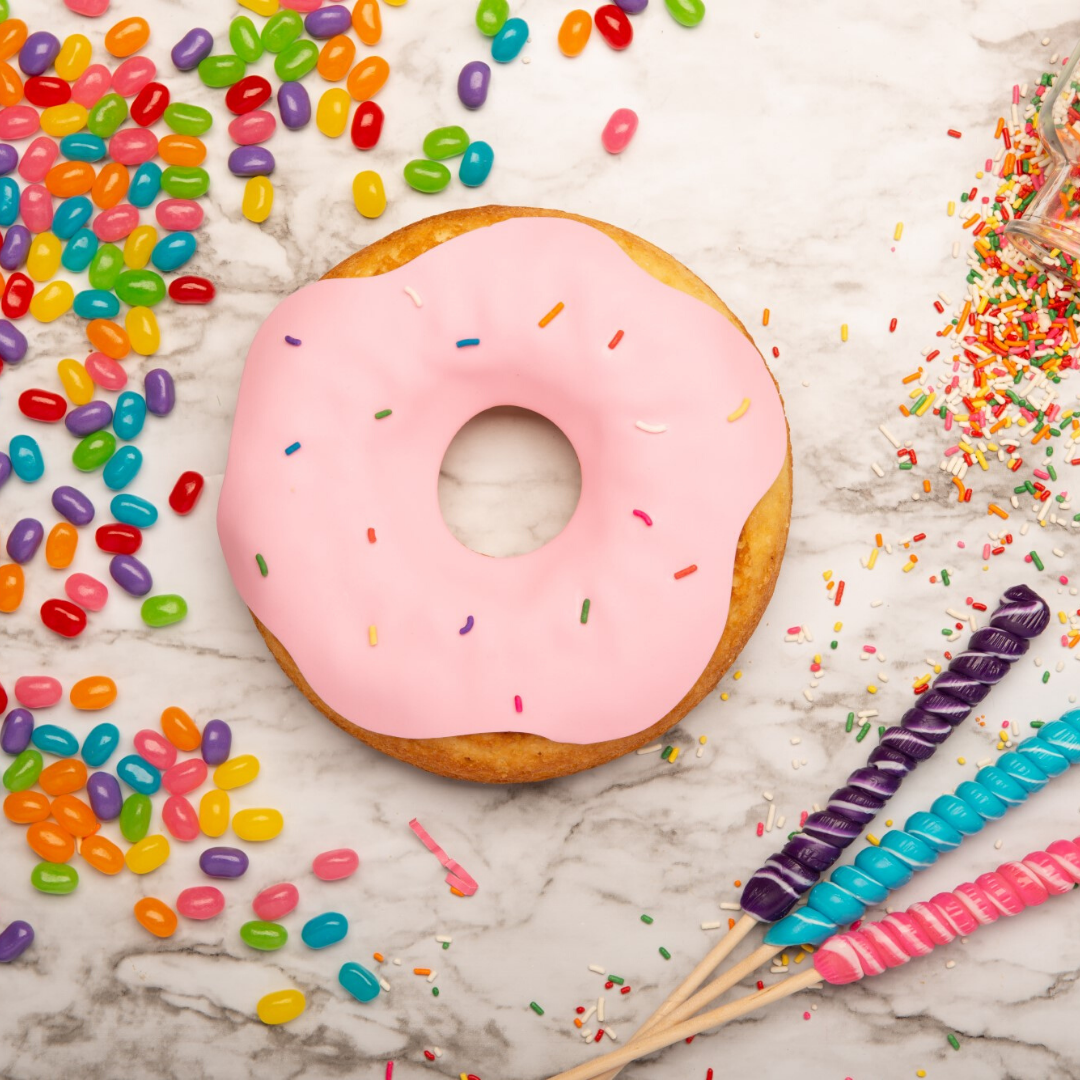 Lifestyle image of Donut shaped decorated cake with pink frosting and sprinkles