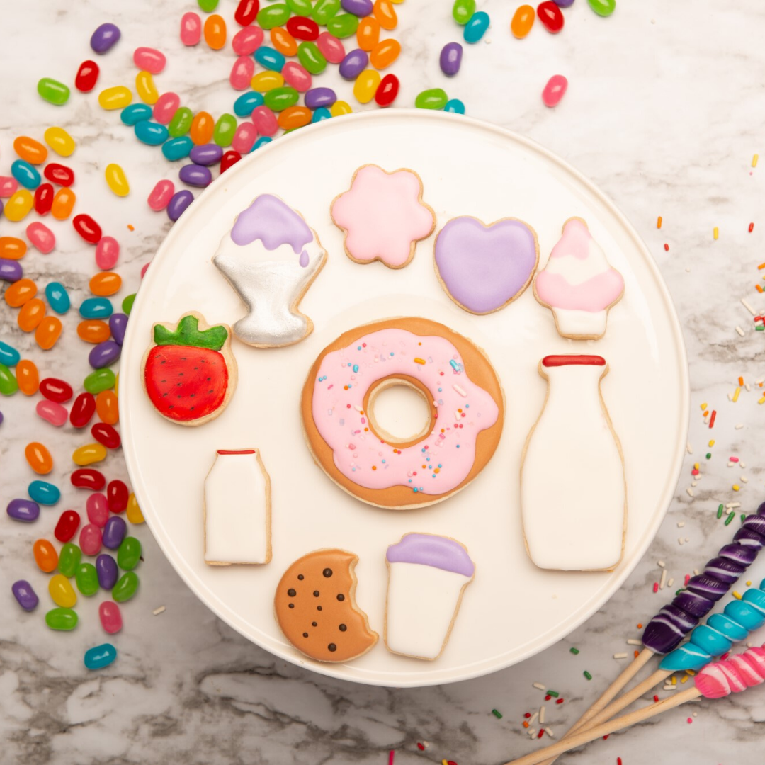 Lifestyle image of : donut, milk bottle, cupcake, milk carton, bitten cookie, heart, flower,  strawberry, coffee cup and ice cream sundae shaped and decorated cookies
