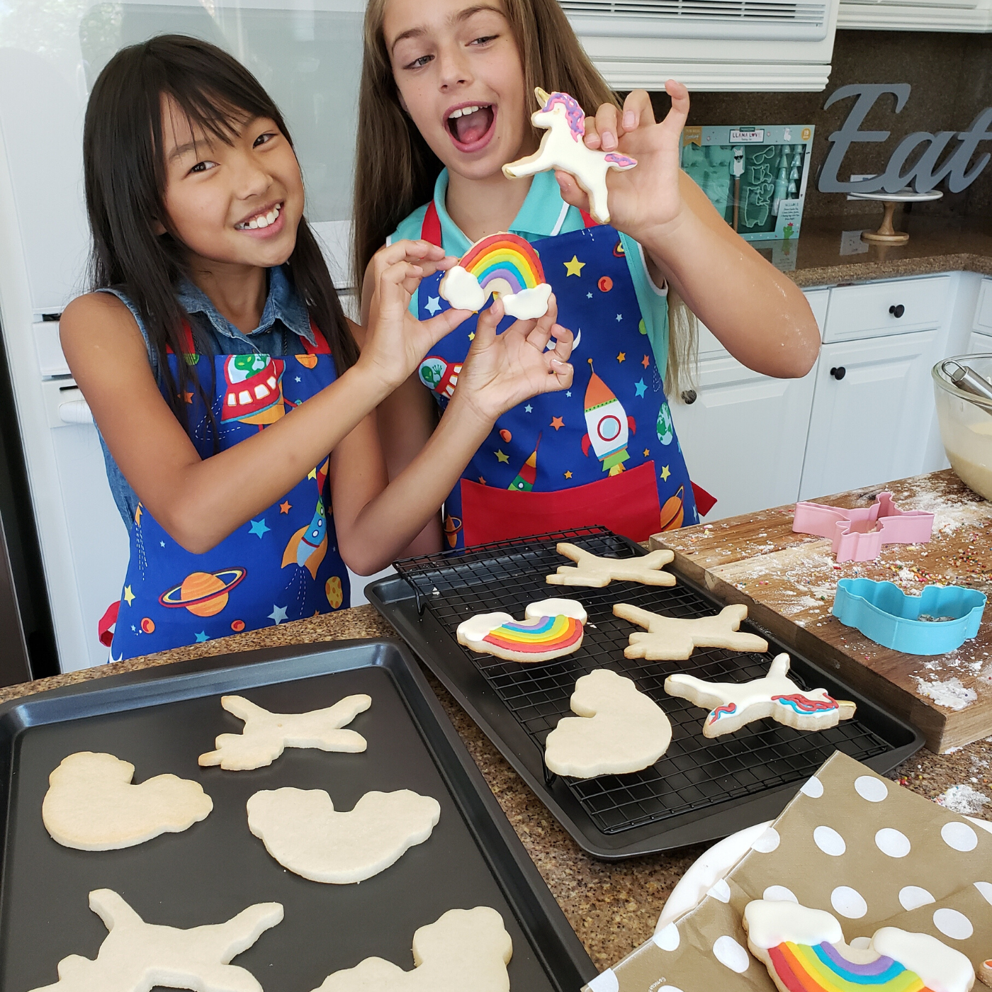 Lifestyle image of two girls showing finished product of unicorn and rainbow cookies.