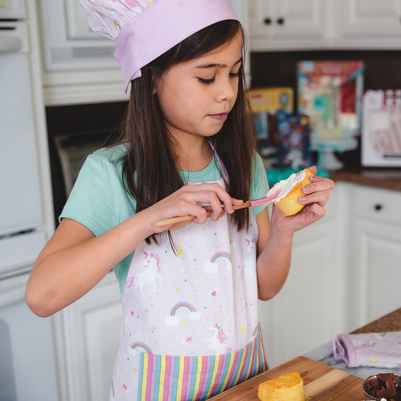 Lifestyle image of girl wearing youth unicorn apron while baking