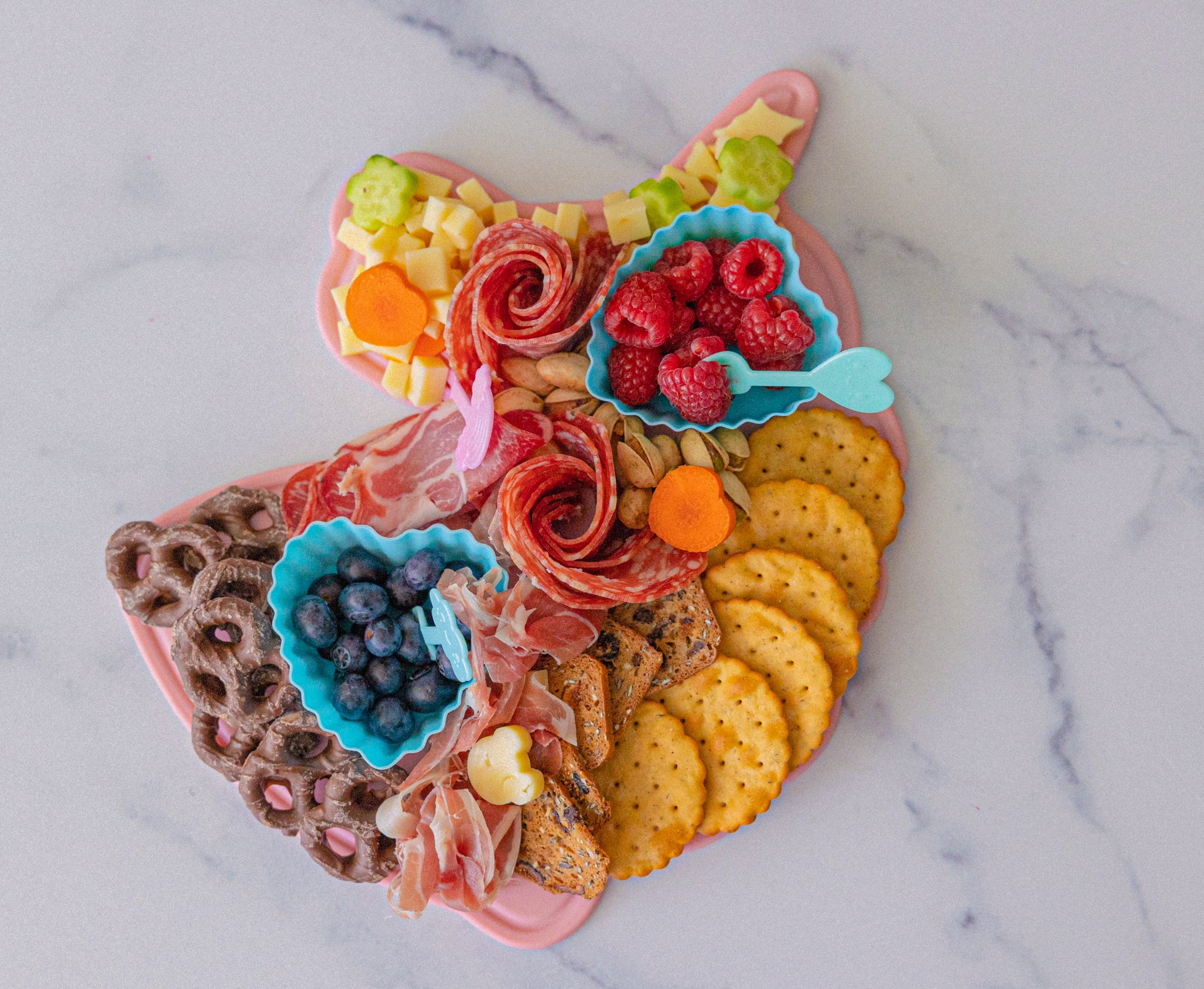 Lifestyle image of Unicorn CHARcuteRIE board that is displaying various fruit, vegetables, meat, and crackers. 