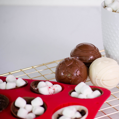 Lifestyle image of 3 complete hot cocoa bombs along with spheres half filled with cocoa bomb toppings such as marshmallows and chocolate chips