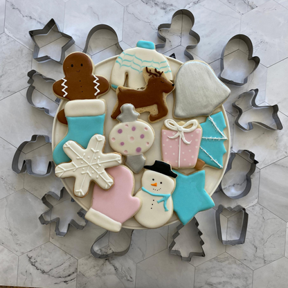 Lifestyle image of completed winter wonderland cookies including a snowman, Christmas tree, snowflake, and more.  