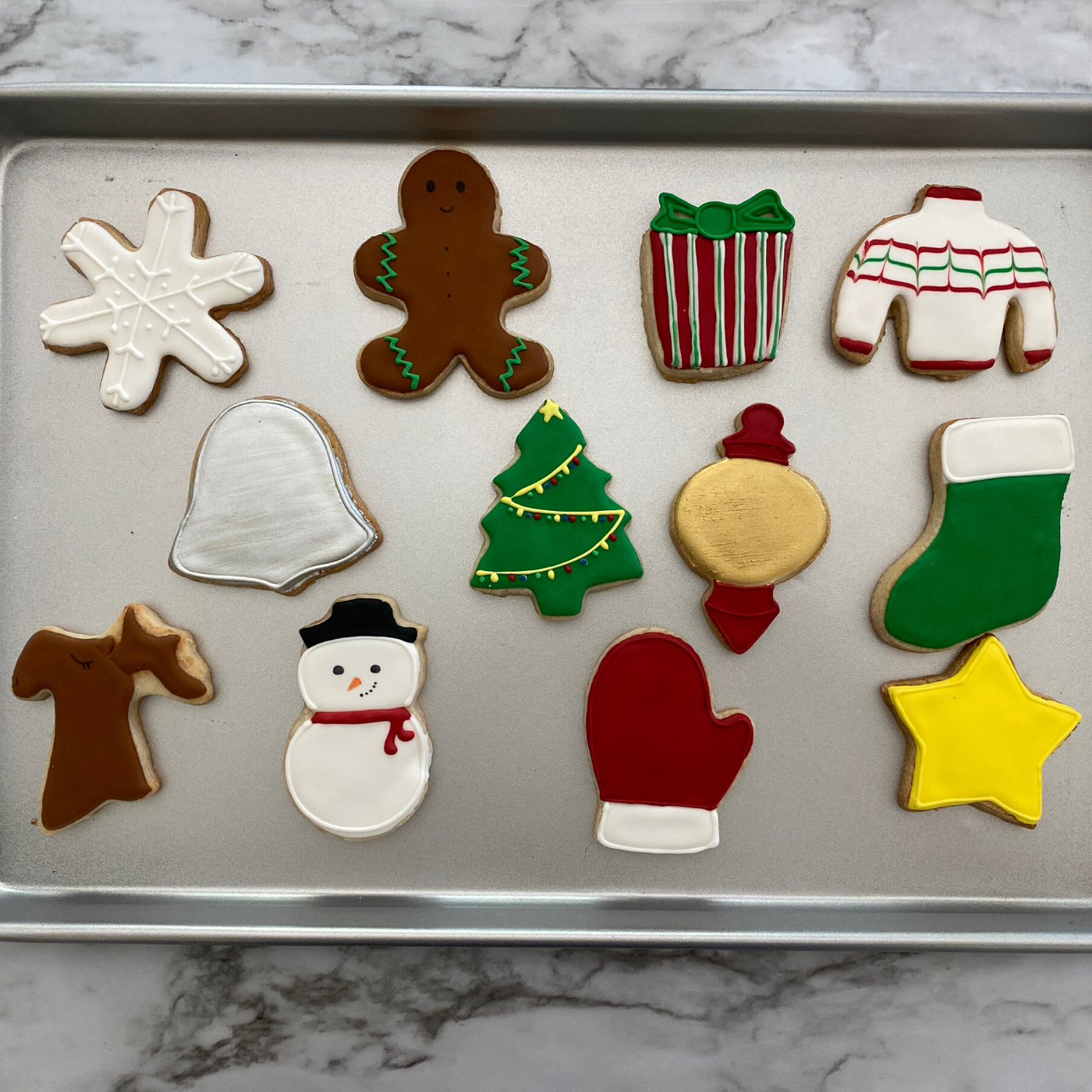 Lifestyle image of completed winter wonderland cookies including a snowman, Christmas tree, snowflake, and more. 