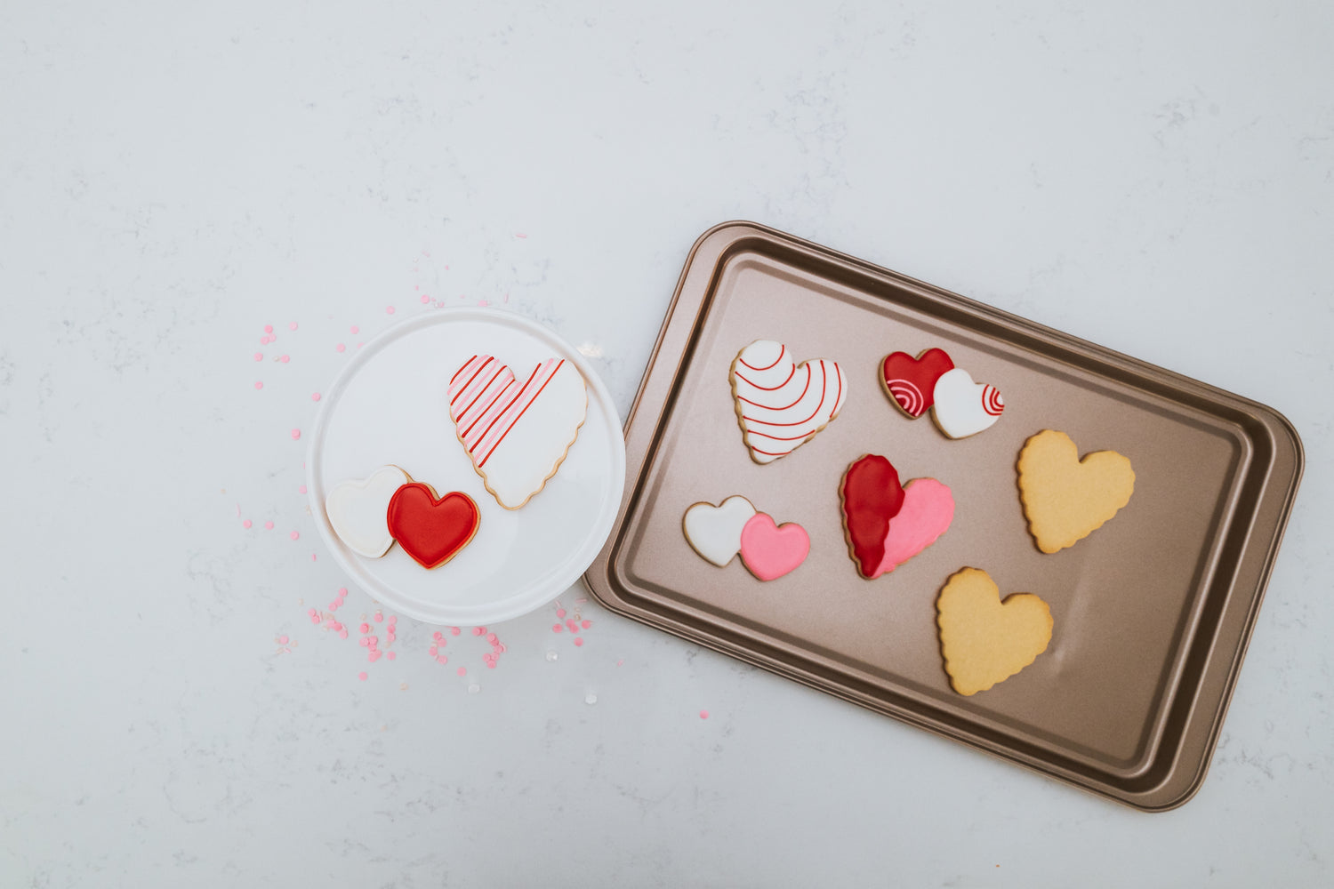 Lifestyle image of decorated heart shaped cookies on a plater and baking sheet