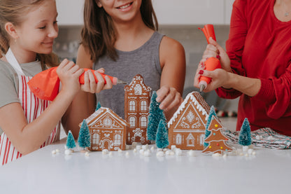 Lifestyle of adult and children decorating gingerbread village made with Make Your Own Gingerbread Village set