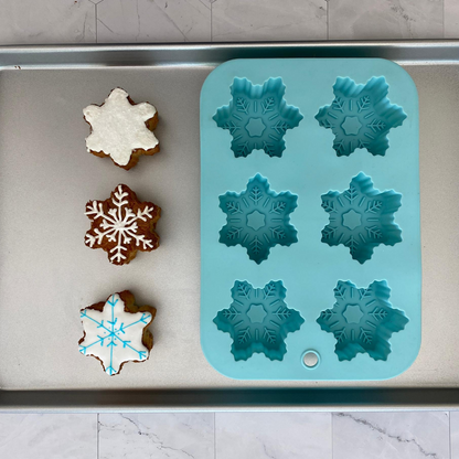 Lifestyle image of Winter Wonderland Snowflake Cupcake Mold with three completed snowflake cupcakes next to it