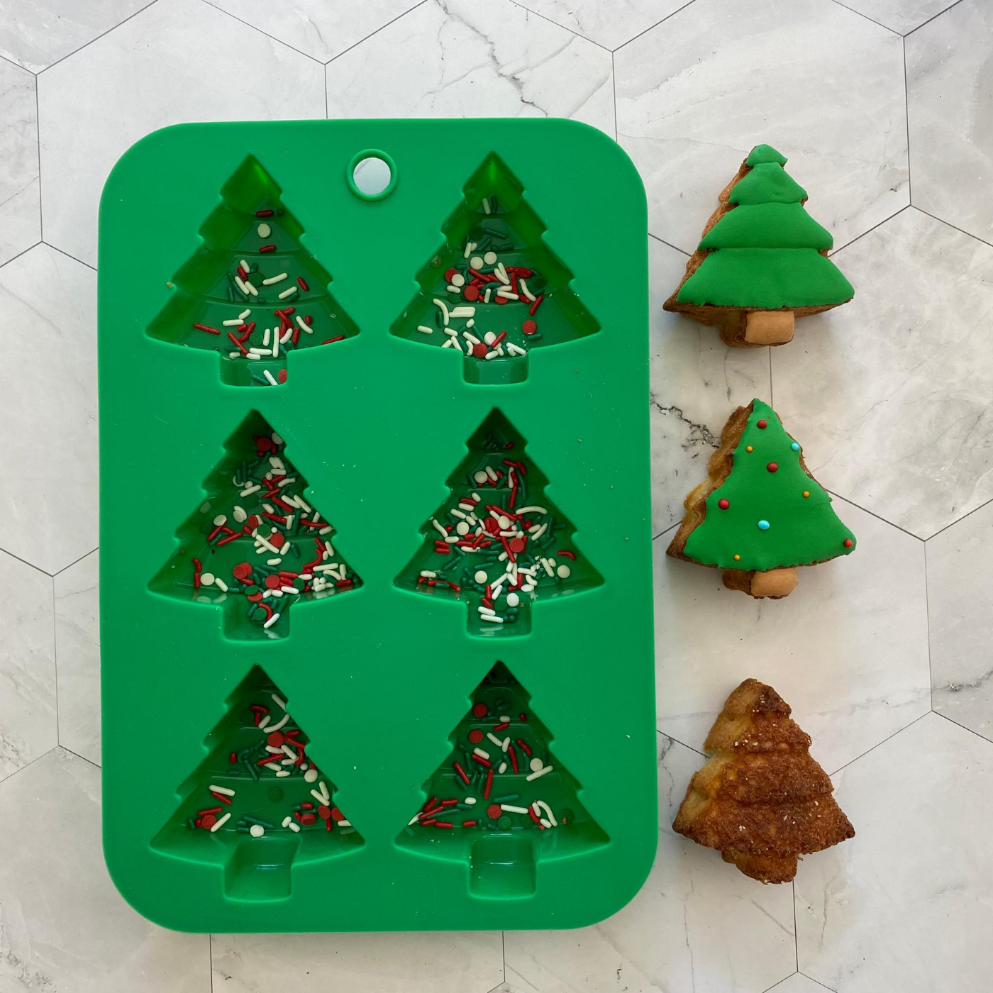 Lifestyle image of Winter Wonderland Holiday Tree Cupcake Mold with three completed cupcakes next to it. 