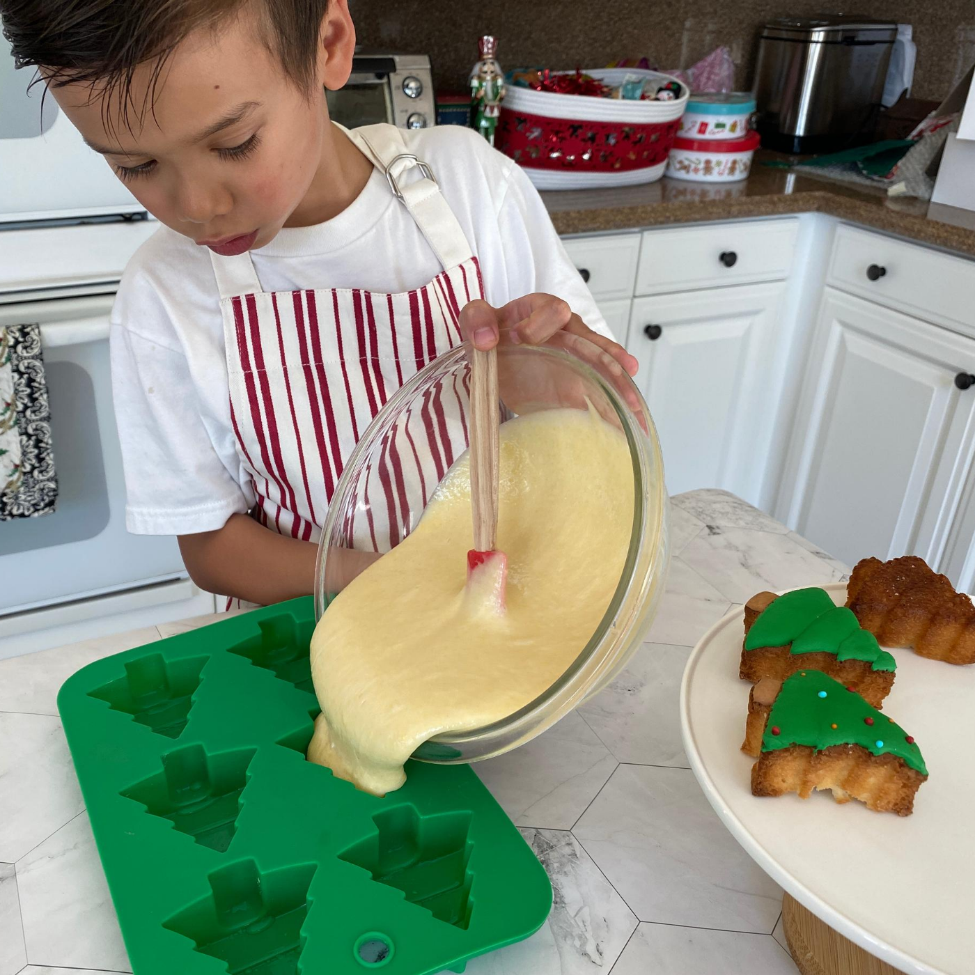 Lifestyle image of a child a child filling the tree cupcake molds with cupcake batter 